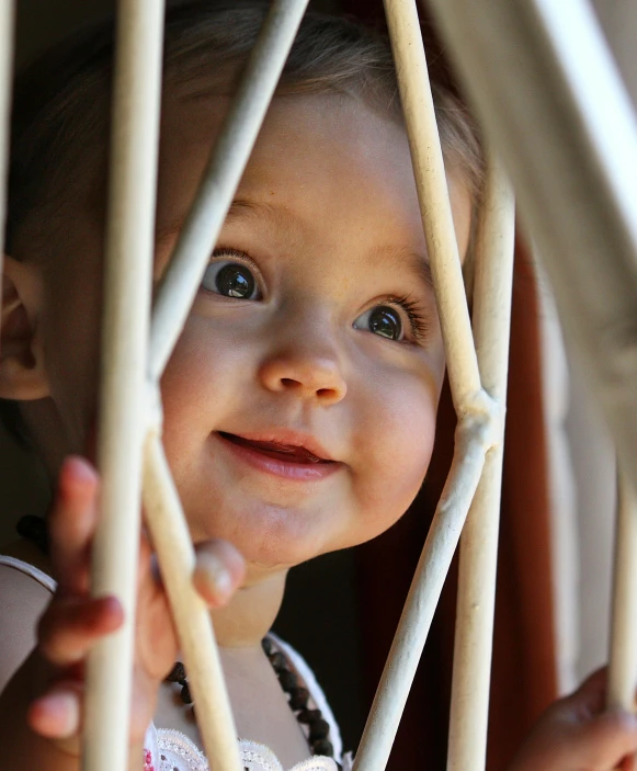 a little girl that is looking out of a window, by Matt Stewart, pexels contest winner, cages, playful smile, square, decorative