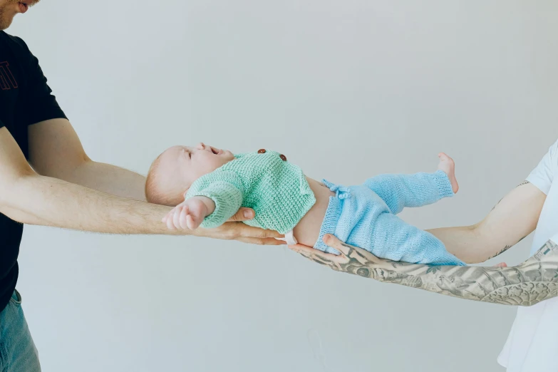 a man holding a baby in his arms, by Alice Mason, pexels contest winner, incoherents, his arms and legs are hanging, with teal clothes, lying down, raising an arm