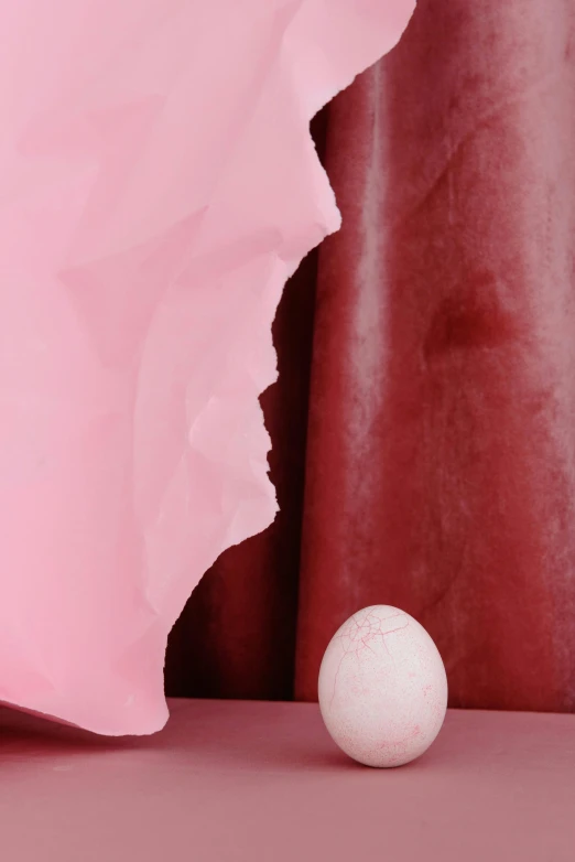 a white ball sitting on top of a pink surface, an abstract sculpture, inspired by Robert Mapplethorpe, chris evans peeks out of an egg, made of silk paper, face and skin is dark red, close-up print of fractured