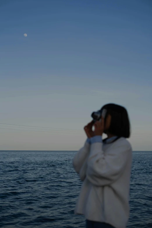 a woman taking a picture of the moon over the ocean, happening, binoculars, louise zhang, distant - mid - shot, profile pose