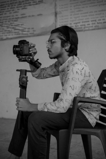 a man sitting on a chair holding a camera, jayison devadas, in black and white, holding a dslr camera, ismail