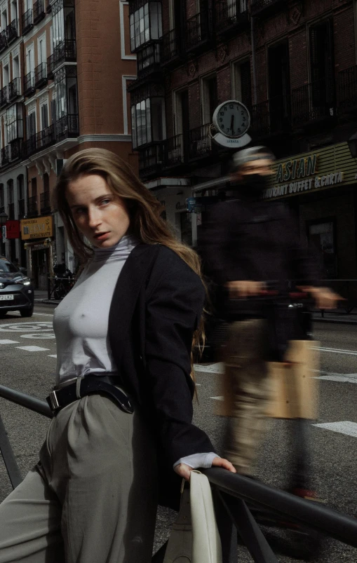 a woman leaning against a railing on a city street, by Luis Molinari, trending on unsplash, photorealism, wearing a turtleneck and jacket, people walking down a street, madrid. extreme long shot, portrait of a female model