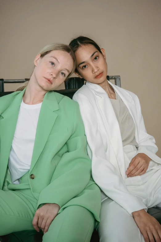 two women sitting next to each other on a bed, inspired by Wang Duo, wearing green suit, wearing white suit, kirsi salonen, jia ruan