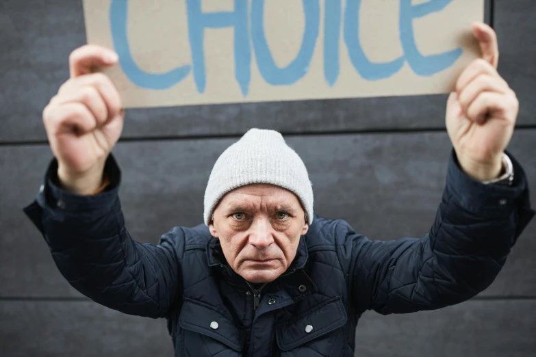 a man holding a sign that says choice, a photo, inspired by Billy Childish, shutterstock, graffiti, anthony hopkins, promo still, limmy, violence