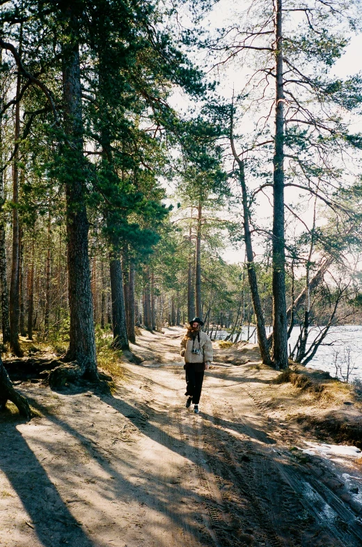 a person walking down a dirt road in the woods, near a lake, kirsi salonen, with trees and rivers, ((forest))