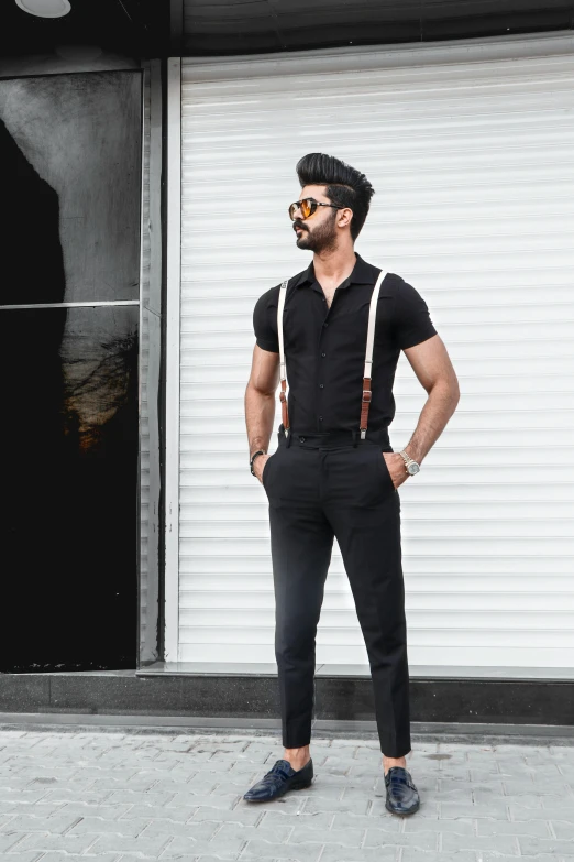 a man standing in front of a store, a colorized photo, trending on pexels, black shirt with red suspenders, indian super model, square, doing an elegant pose