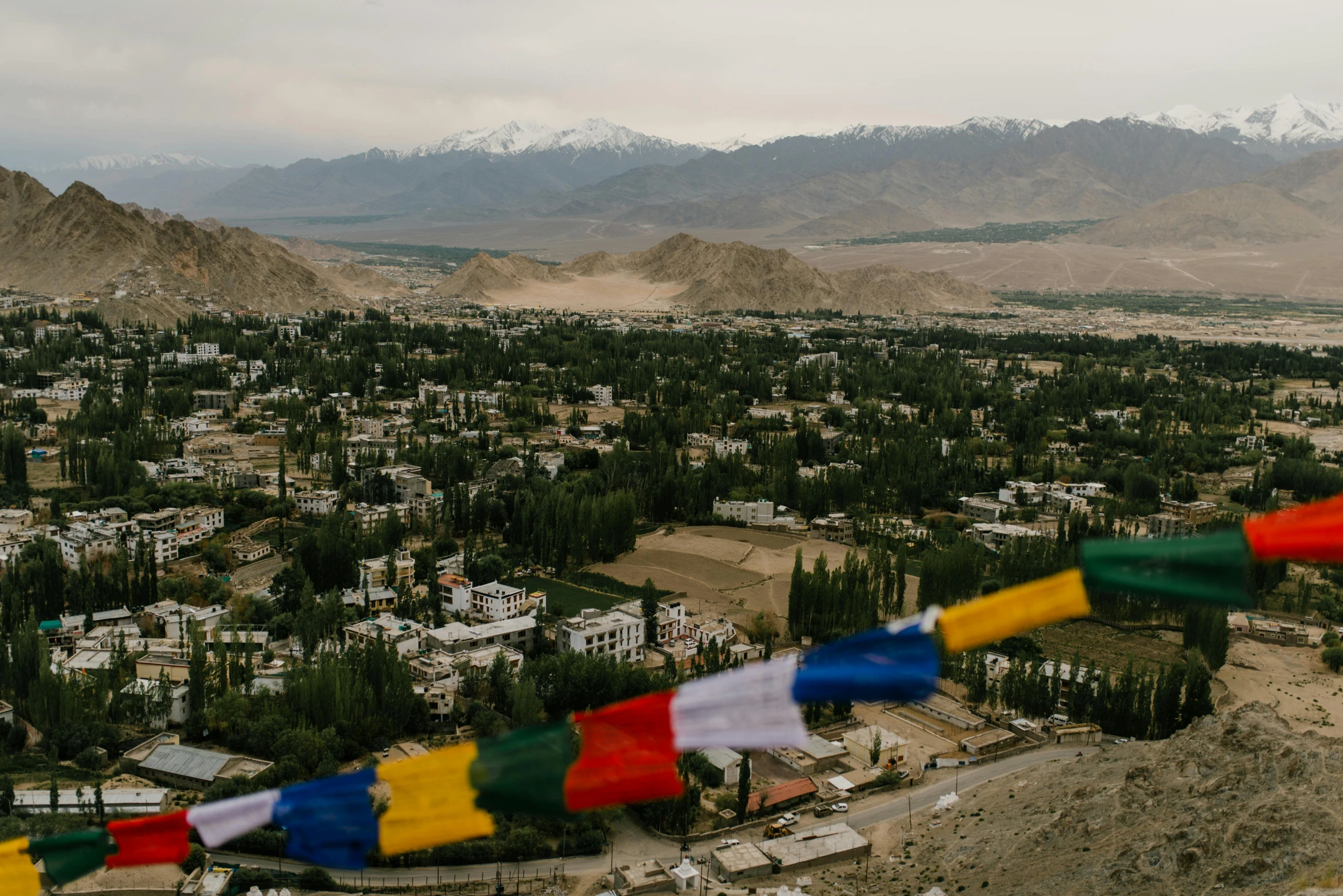 a view of a town with mountains in the background, a portrait, unsplash contest winner, hurufiyya, prayer flags, background image, wide high angle view, india