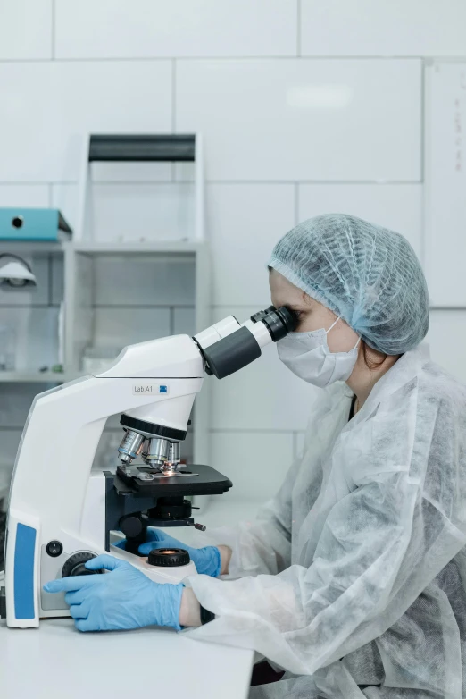 a woman in a lab coat looking through a microscope, surgical gown and scrubs on, trending photo, thumbnail, mining