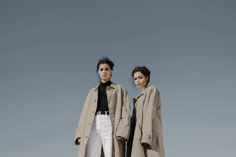 a couple of women standing next to each other, an album cover, unsplash, bauhaus, trench coat, 15081959 21121991 01012000 4k, sky view, shot with sony alpha