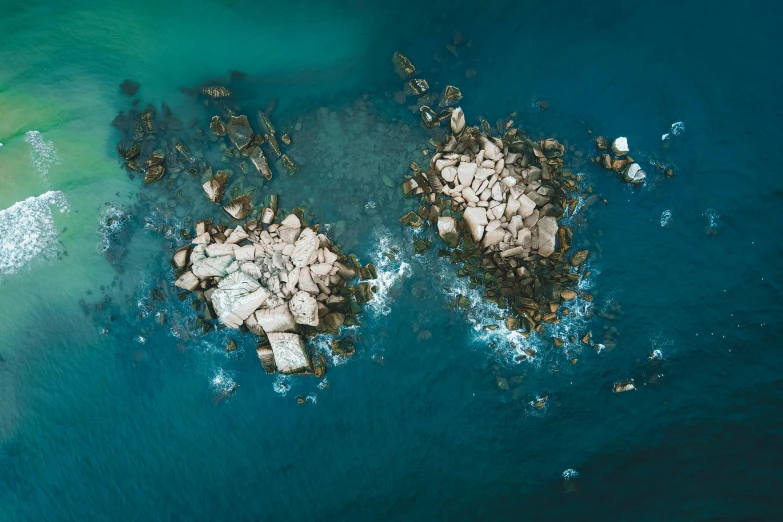 a couple of rocks sitting on top of a body of water, by Adam Marczyński, pexels, aerial illustration, reefs, teals, brown