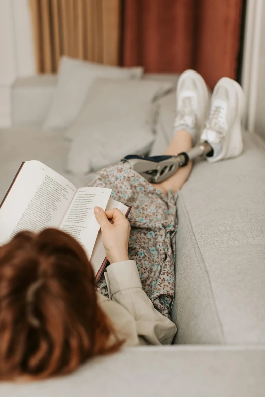 a woman laying on a couch reading a book, pexels contest winner, prosthetic leg, casually dressed, with high detail, studious