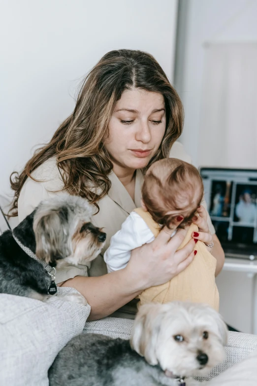 a woman sitting on a bed holding a baby and two dogs, trending on pexels, modernism, mourning family, in front of a computer, embracing, professional photo