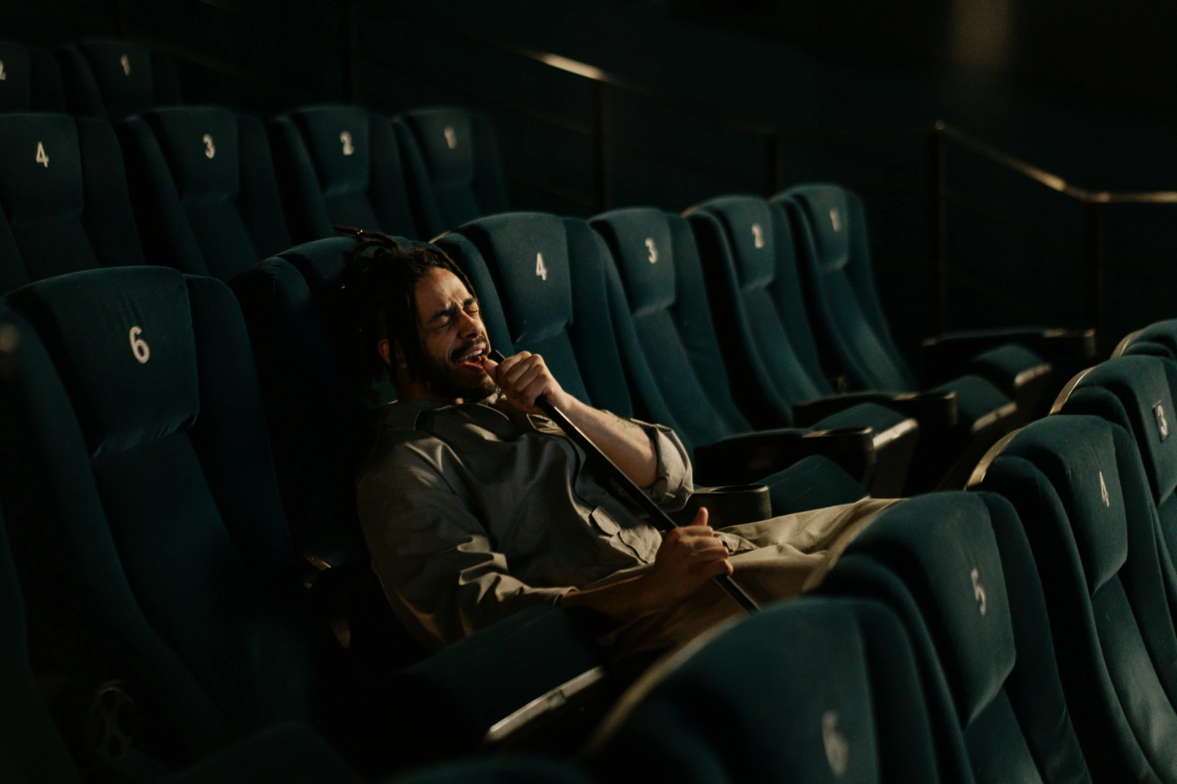 a man sitting in a theater talking on a cell phone, by Elsa Bleda, pexels contest winner, serial art, photorealistic logan movie still, sleepy, cinematic colour grading, sitting in a chair