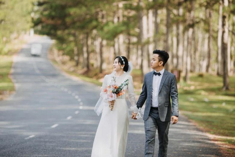 a man and a woman walking down a road, inspired by Ruth Jên, unsplash, wedding, ao dai, “ iron bark, in front of a forest background