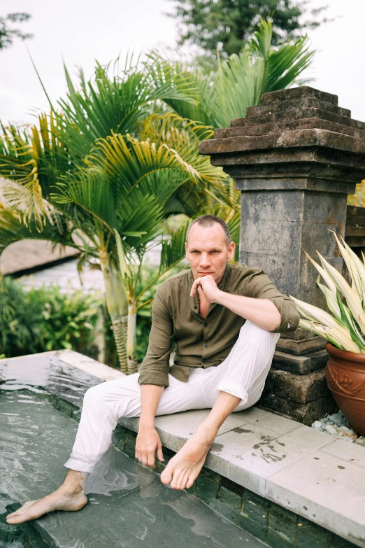 a man sitting on the edge of a pool, a portrait, inspired by Petr Brandl, unsplash, renaissance, white pants, bali, shaved sides, lush green