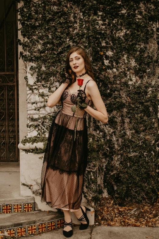 a woman in a dress standing in front of a building, an album cover, by Robbie Trevino, pexels contest winner, renaissance, holding a rose, southern gothic scene, young beautiful amouranth, 1 9 1 0 s style