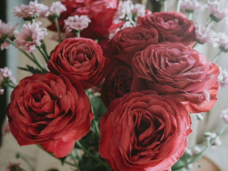 a vase filled with red roses sitting on a table, by Carey Morris, pexels contest winner, zoomed in, slightly tanned, maroon red, close up shot from the side