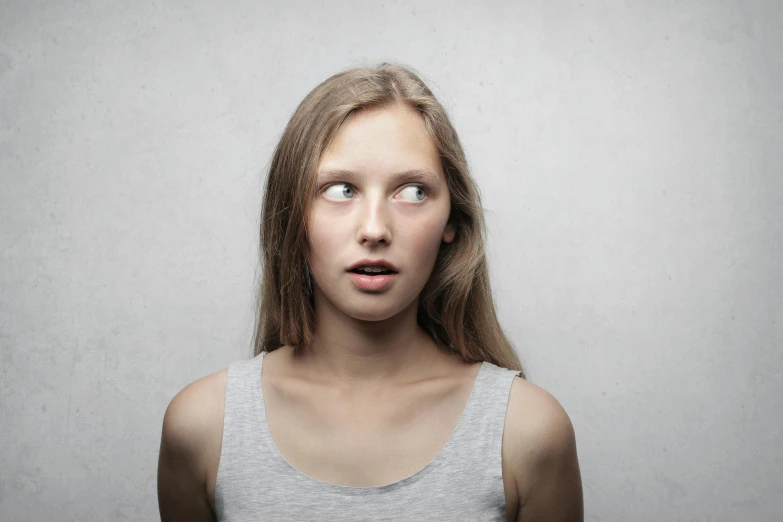 a woman with a surprised look on her face, by Adam Marczyński, trending on pexels, incoherents, on grey background, teenage, looking up, pale-skinned