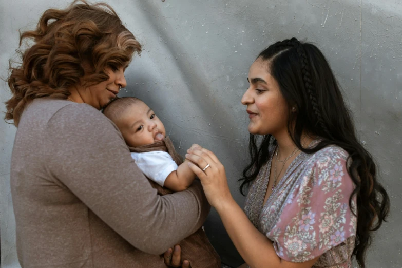 a woman standing next to a woman holding a baby, pexels contest winner, an olive skinned, lesbian, profile image, middle eastern skin