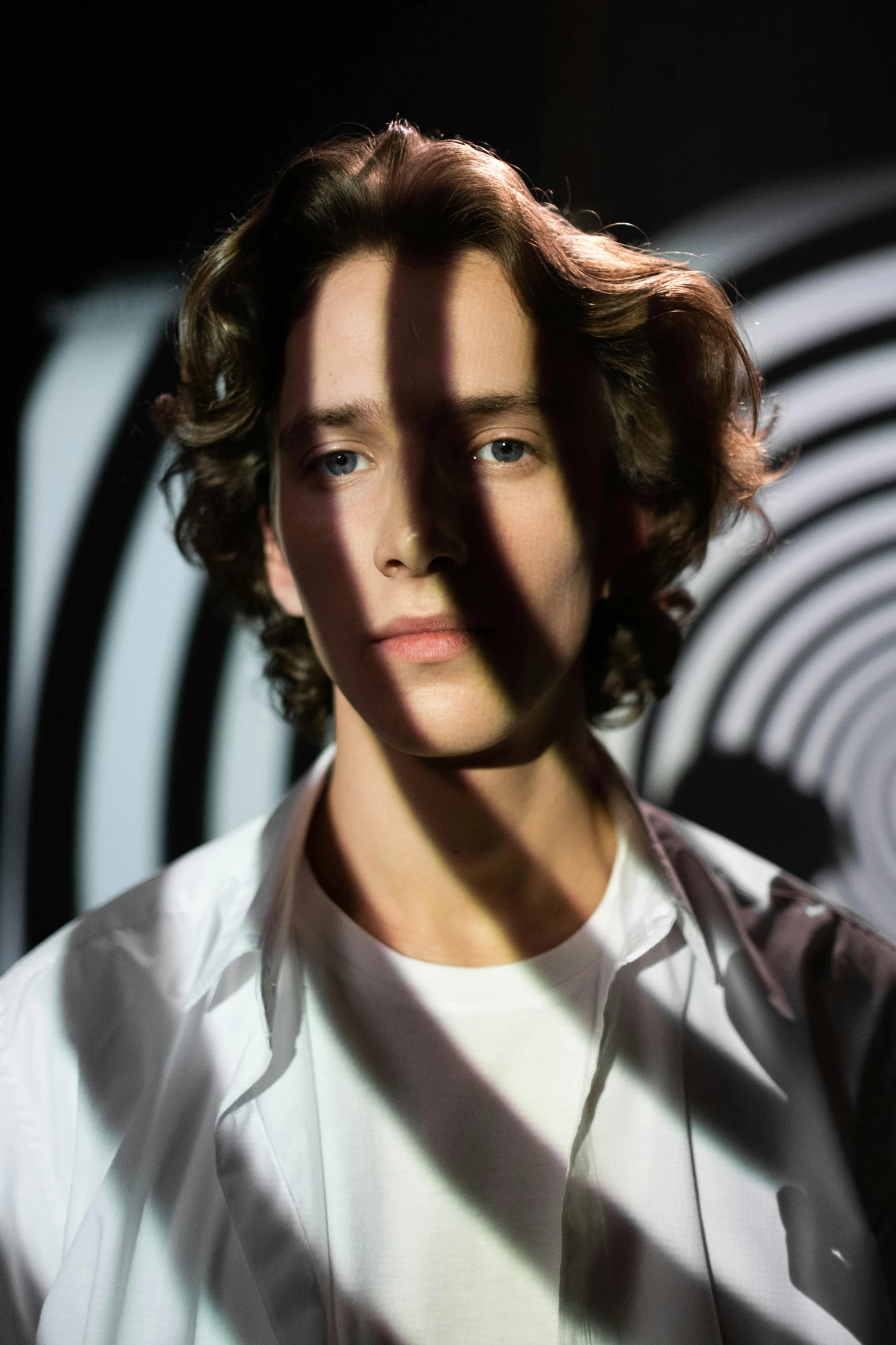 a man standing in front of a black and white background, an album cover, inspired by Thomas Wijck, hyperrealism, brightly glowing eyes, teen boy, curls, androgynous person