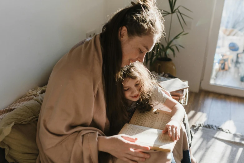 a woman reading a book to a little girl, pexels contest winner, wearing brown robes, connection rituals, over the shoulder, cardboard