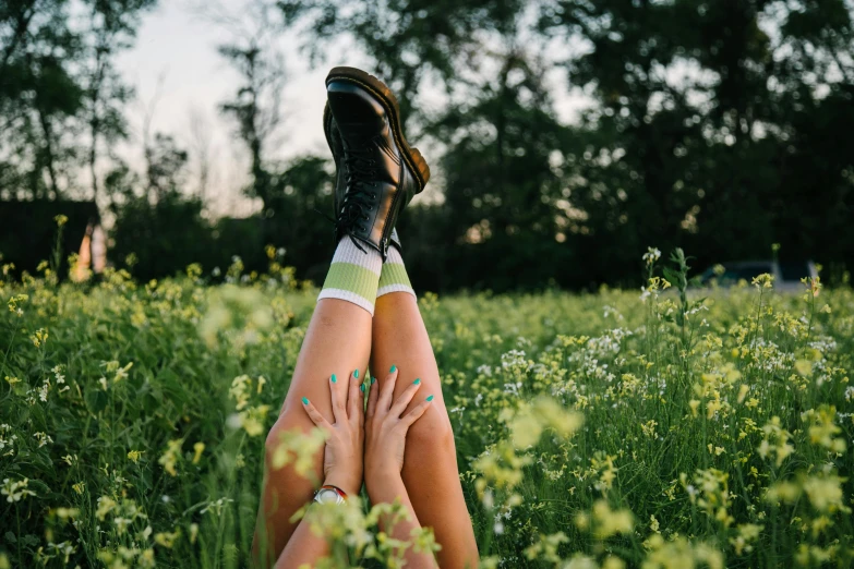 a woman laying on top of a lush green field, inspired by Elsa Bleda, trending on pexels, aestheticism, knee high socks, buttercups, black and green, doc marten boots