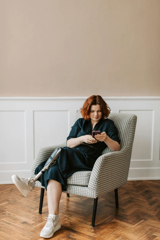 a woman sitting in a chair looking at her phone, prosthetic limbs, ( redhead, jovana rikalo, high quality photo