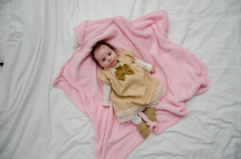 a baby wrapped in a pink blanket on a bed, pexels, baroque, square, beige, little elf girl, high angle shot