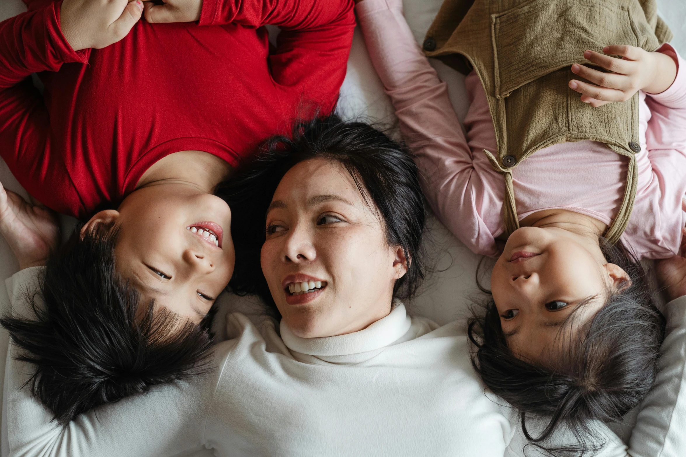 a group of people laying on top of a bed, by Carey Morris, pexels contest winner, incoherents, an indonesian family portrait, three women, ethnicity : japanese, smiling at each other