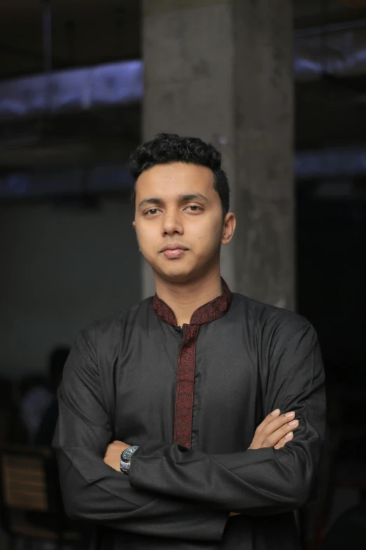 a young man standing with his arms crossed, inspired by Bikash Bhattacharjee, wearing a black shirt, islamic, profile image, androgynous person