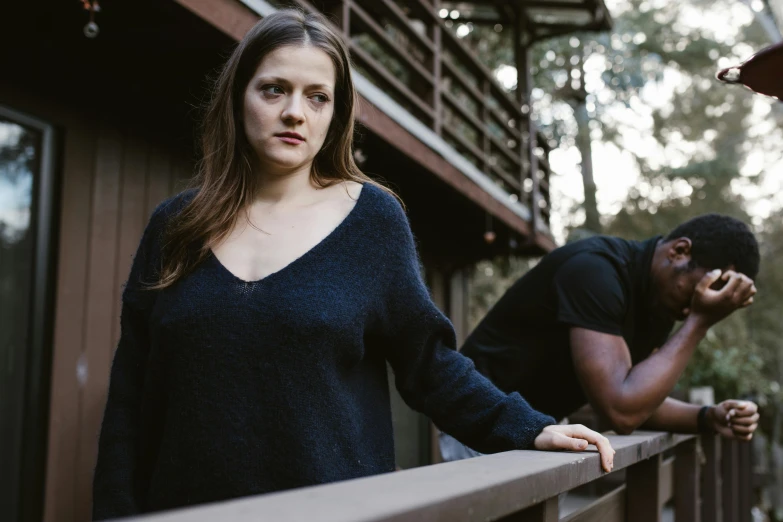 a woman leaning on a railing next to a man, wearing a dark sweater, background image, menacing, stood outside a wooden cabin