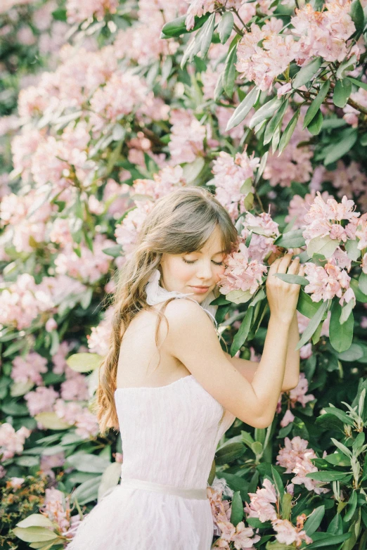 a woman standing in front of a bush of flowers, trending on unsplash, romanticism, girl with brown hair, pink pastel, photoshoot for skincare brand, angelina stroganova