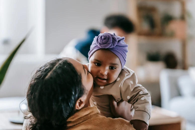 a woman holding a baby in her arms, pexels contest winner, varying ethnicities, manuka, wearing a purple cap, at home