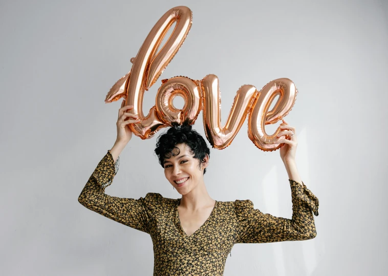 a woman holding up a balloon shaped like the word love, an album cover, pexels, rose gold, official product photo, rebecca sugar, various posed