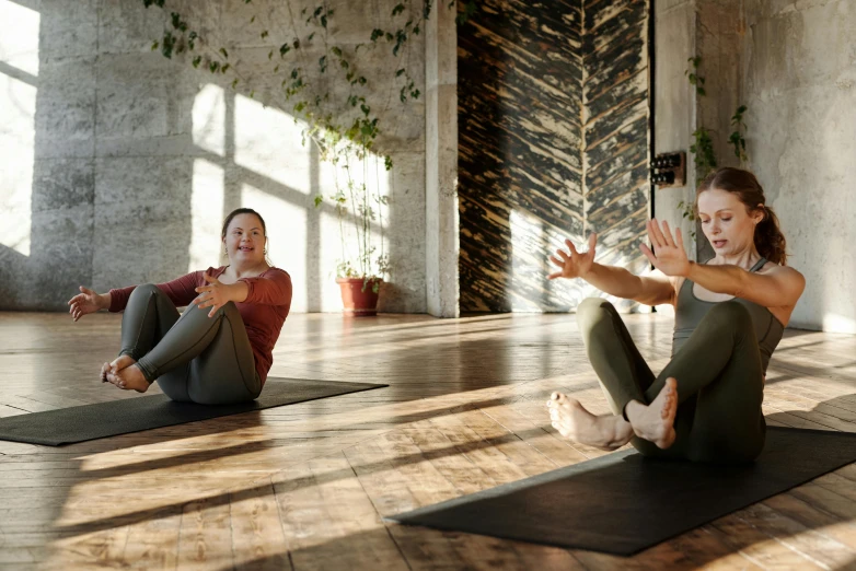 a couple of women sitting on top of a yoga mat, by Emma Andijewska, pexels contest winner, renaissance, local gym, filled with natural light, thumbnail, earthy