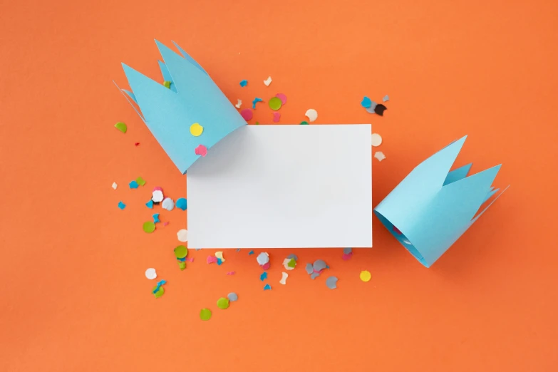 a paper crown and confetti sprinkles on an orange background, by Julia Pishtar, pexels contest winner, blue themed, card template, miscellaneous objects, background image