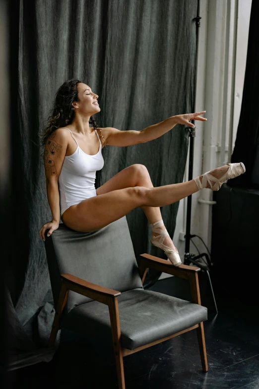 a woman sitting on top of a chair next to a window, by Elizabeth Polunin, pexels contest winner, arabesque, wearing white leotard, excited, sits on a finger, gif