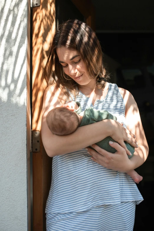 a woman holding a baby in her arms, pexels contest winner, leaning on door, wearing a cute top, greens), nursing