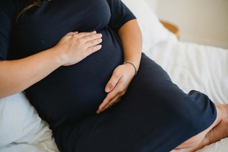 a pregnant woman sitting on top of a bed, unsplash, holding hand, navy, manuka, obese )