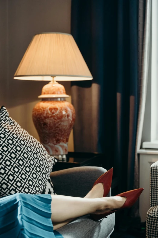 a woman sitting on a couch reading a book, inspired by Constantin Hansen, baroque, orange lamp, maroon and blue accents, warm lantern lighting, monochrome