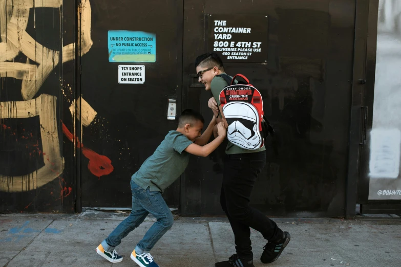 a man helping a young boy with a backpack, by Thomas Furlong, pexels contest winner, street art, storm trooper, posing for a fight, los angeles ca, back to school comedy