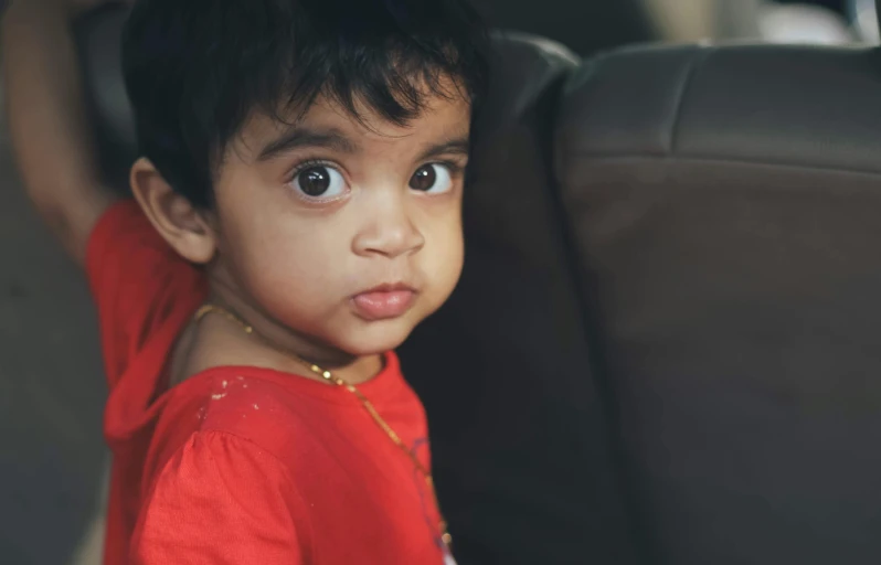 a little boy sitting in the back seat of a car, pexels contest winner, hurufiyya, indian girl with brown skin, his eyes glowing red, sitting on couch, prominent big eyes