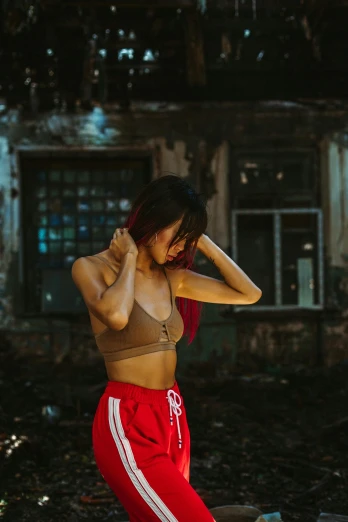 a woman in red pants standing in front of a building, an album cover, inspired by Elsa Bleda, pexels contest winner, graffiti, sports bra, beautiful asian girl, sweaty and dirty, croptop
