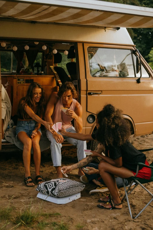 a group of people sitting around a camper van, by Lee Loughridge, pexels contest winner, renaissance, playing cards, slightly tanned, aboriginal australian hipster, ( ( ( ( kauai ) ) ) )