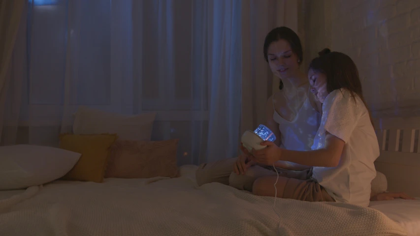 a woman sitting on top of a bed holding a nintendo wii game controller, a hologram, by Adam Marczyński, pexels, video art, in the bedroom at a sleepover, with a kid, soft lighting 8k, woman holding another woman