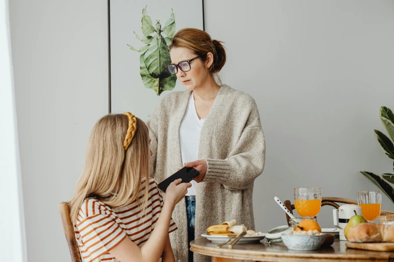 a woman standing next to a woman sitting at a table, by Emma Andijewska, trending on pexels, happening, caring fatherly wide forehead, digital glasses, girl making a phone call, styled hair