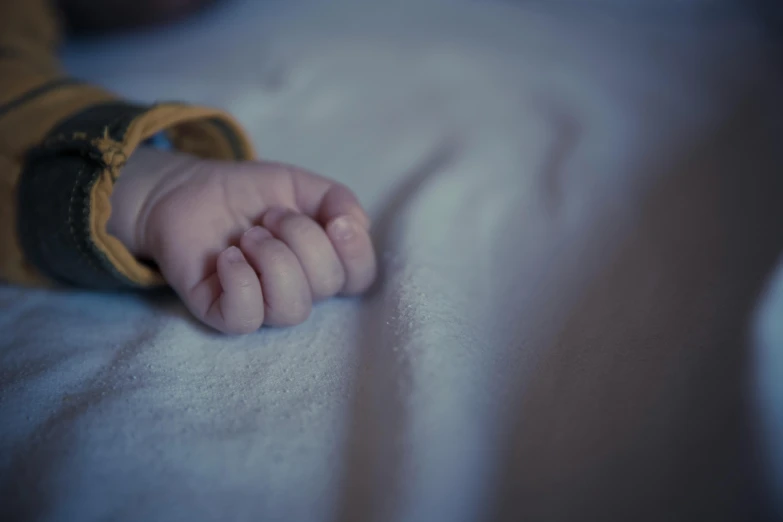 a close up of a baby's hand on a bed, unsplash, coloured, brooding, closeup portrait shot, lying down