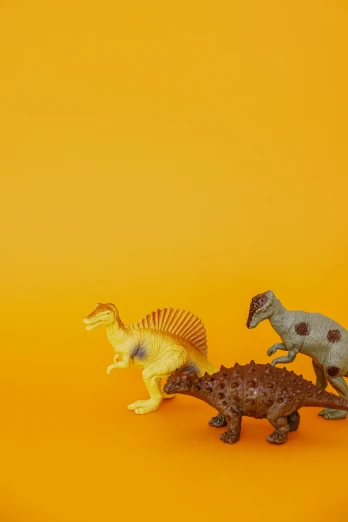 a couple of toy dinosaurs standing next to each other, by Sam Havadtoy, trending on unsplash, yellow backdrop, vintage, photographed for reuters, jen atkin