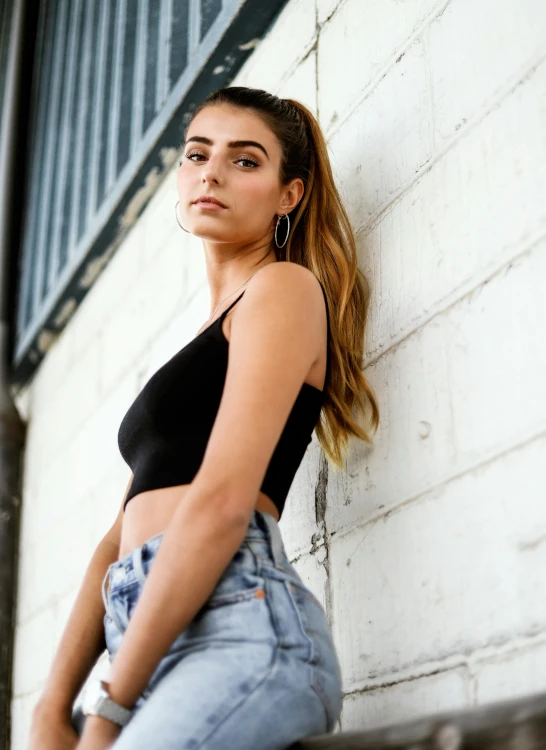 a woman leaning against a white brick wall, trending on pexels, wearing a cropped black tank top, asher duran, promotional image, profile image