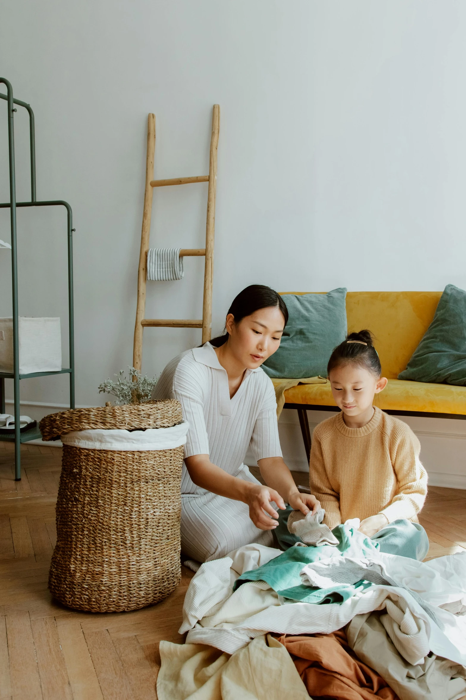 a woman sitting on the floor next to a child, by Ruth Jên, pexels contest winner, minimalism, with an easter basket, inspect in inventory image, wearing a linen shirt, asian female
